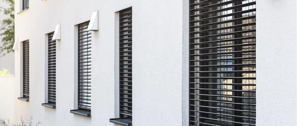 Mehrere Fenster mit modernen außenliegenden Jalousien an einer weißen Fassade als Sonnenschutz und Sichtschutz.